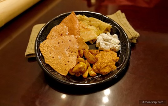 Traditional Naan, Onion Kulcha, and Papadum Breads plated with Roasted Pepper Hummus, Raita and Garlic-Ginger Pickle Dips.