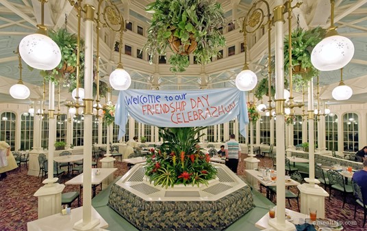 The "Friendship Day Celebration" banner hangs near the center of each of the dining areas. The center feature itself is a mix of planter, air conditioning system, and bench style seating