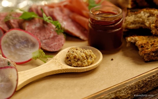 The coarse grain mustard grain mustard is presented on a little wooden spoon.