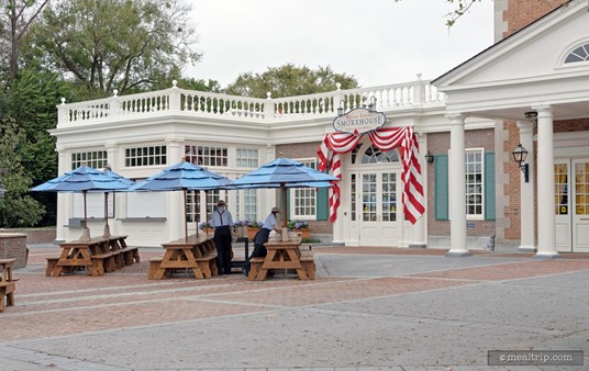 Walking up to the Regal Eagle Smokehouse from the west. There are a few outdoor seating options, and the main entrance is under the draped red and white curtain banner.