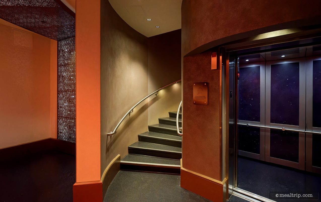 Past the first check-in point on the ground level there's winding stairs that lead up to Geo-82 and a small Otis elevator. Between the two – there's a small, copper colored placard with some words etched in it. Behind me, there's a curved wall with a giant G logo placed in the center.