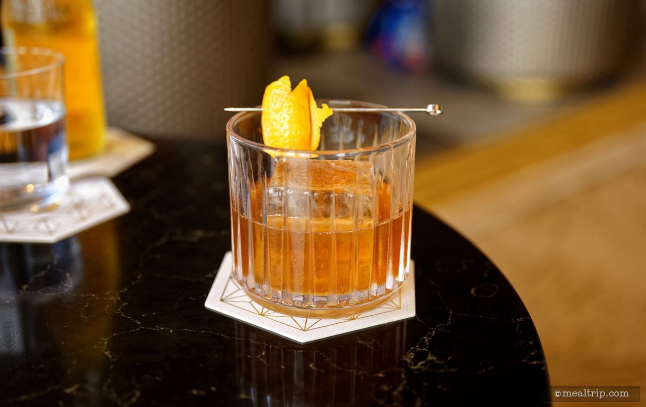 This is one of the Featured Cocktails, a Brown Butter Old-Fashioned ($28.00 as purchased, Summer 2025). The cocktail is said to feature Woodford Reserve Double Oaked Bourbon, Brown Butter, Maple, and Mexican Chocolate Bitters from the Hella Cocktail Company.